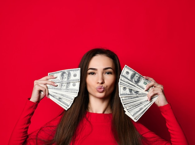 Jovem mulher bonita de vestido vermelho se escondendo atrás de um monte de notas de dinheiro