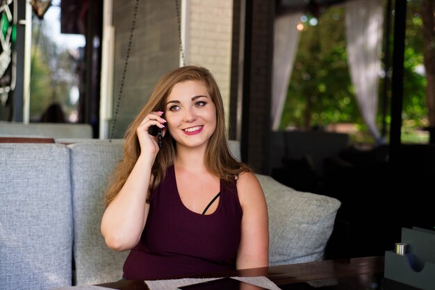 Jovem mulher bonita do tamanho positivo com tabuleta e telefone em um restaurante.