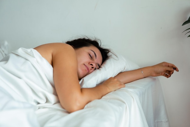 Jovem mulher bonita dormindo na cama com lençóis brancos