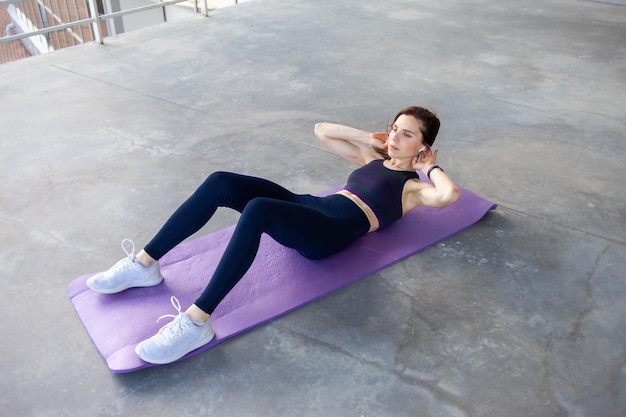 Jovem mulher bonita e em forma fazendo abdominais enquanto deitada em um tapete em um chão de concreto corpo perfeito músculos abdominais de aço