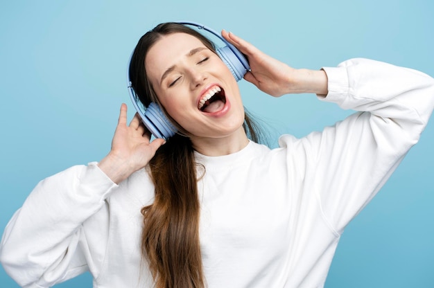 Jovem mulher bonita e emocional usando fones de ouvido sem fio ouvindo música cantando canção