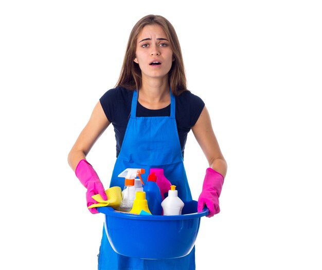 Jovem mulher bonita em camiseta azul e avental com luvas segurando coisas de limpeza na bacia azul