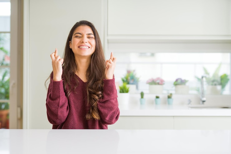 Foto jovem mulher bonita em casa sorrindo cruzando os dedos com esperança e olhos fechados sorte e conceito supersticioso