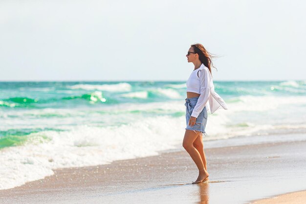 Jovem mulher bonita em férias na praia caminhando ao lado do mar