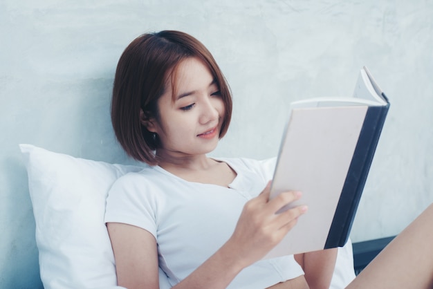 Jovem mulher bonita em lingerie branca lendo livro na cama