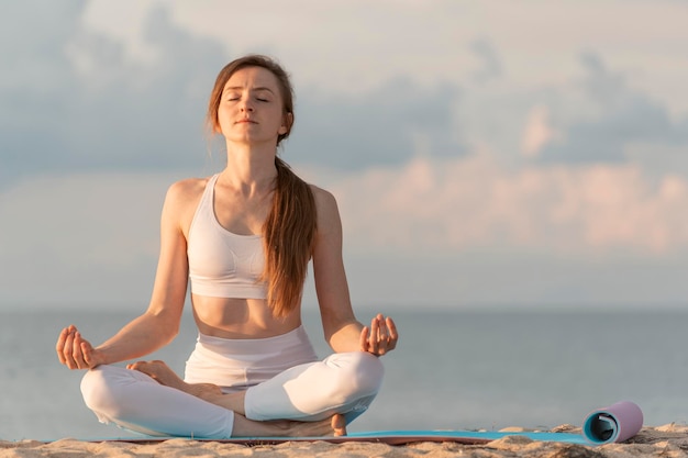 Jovem mulher bonita em posição de lótus meditação na praia Mulher praticando ioga no fundo do mar