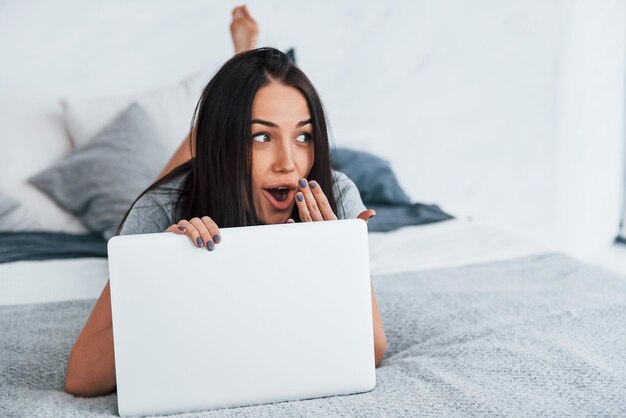 Jovem mulher bonita em roupas casuais, deitada em casa sozinha com o laptop.