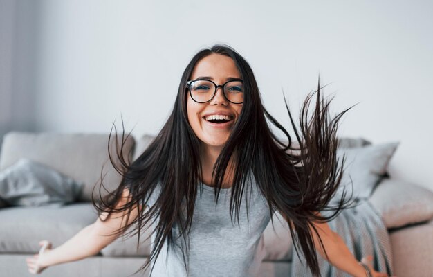 Jovem mulher bonita em roupas casuais e óculos se diverte em casa sozinha.