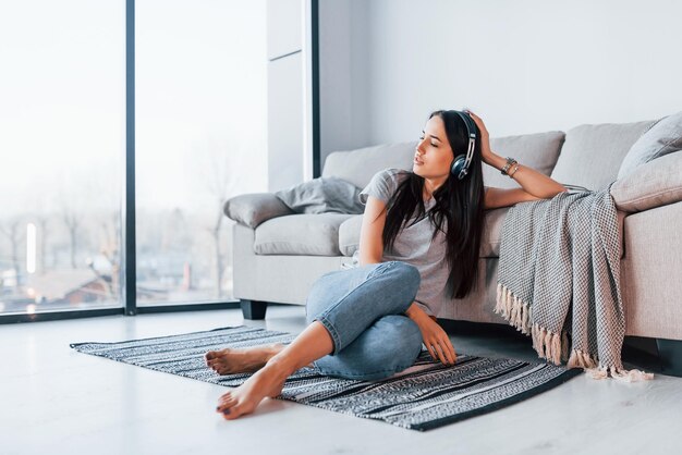 Jovem mulher bonita em roupas casuais, sentado em casa sozinho e ouvindo a música em fones de ouvido.