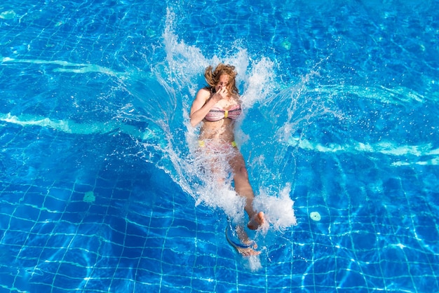 Jovem mulher bonita em traje de banho pulando na piscina com um esguicho