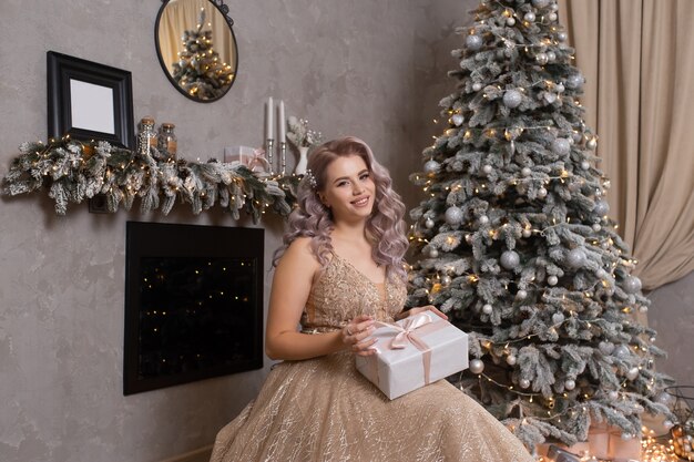 Jovem mulher bonita em um elegante vestido de noite sentada perto da árvore de Natal, ano novo