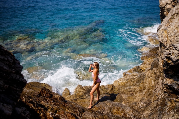 Jovem mulher bonita em um maiô fica em uma praia rochosa do mar Mediterrâneo. O conceito de recreação marítima. Foco seletivo