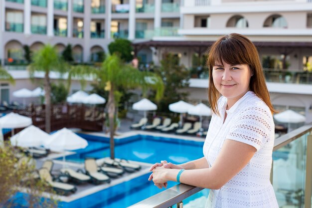 Jovem mulher bonita em um vestido branco posando na varanda de um hotel moderno