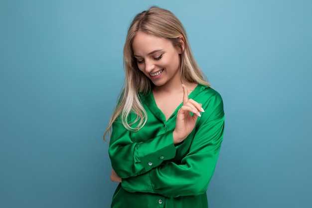 Jovem mulher bonita em uma camisa verde olha timidamente para o chão em um fundo de estúdio azul