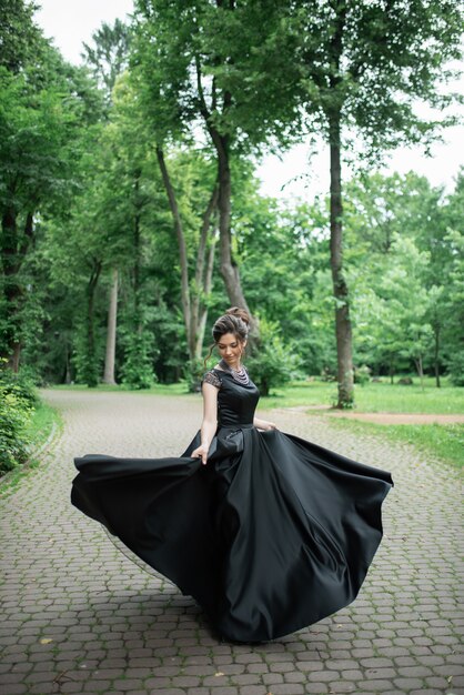 Jovem mulher bonita está girando em um vestido preto no parque. O vestido está maravilhosamente em desenvolvimento.