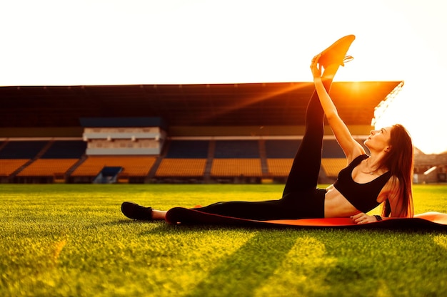 Jovem mulher bonita fazendo alongamento ioga no estádio no pôr do sol horário de verão