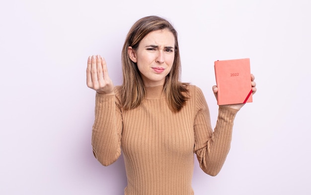 Jovem mulher bonita fazendo gesto capice ou dinheiro dizendo para você pagar o conceito de agenda