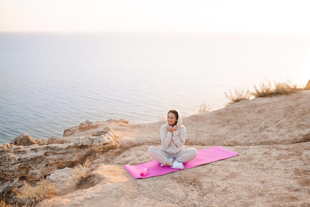 Jovem mulher bonita fazendo pose de ioga usar prática de terno esporte sobre fundo de mar de natureza. Estilo de vida saudável. Garota malha ao ar livre.