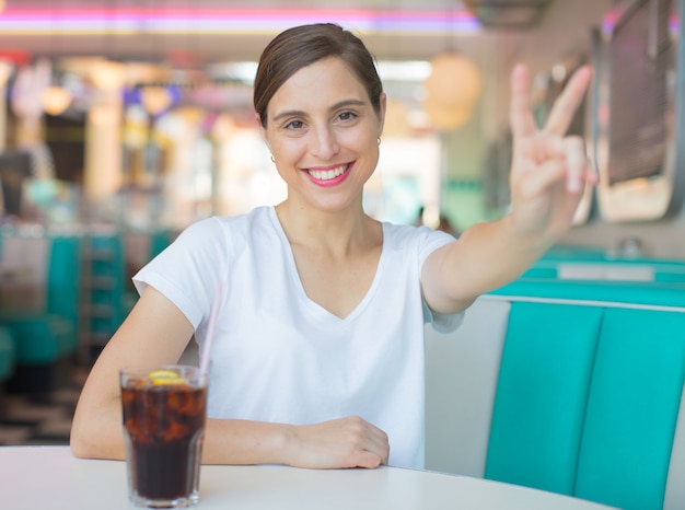 Jovem mulher bonita feliz e satisfeito bebendo uma cola em um restaurante de jantar americano