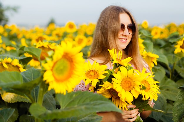 Jovem mulher bonita fica entre os girassóis florescendo