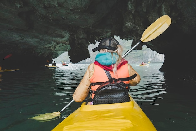 Jovem mulher bonita flutuando em um caiaque na caverna de água A garota remando os remos no fundo da bela paisagem do mar no rio subterrâneo Esportes ativos na água