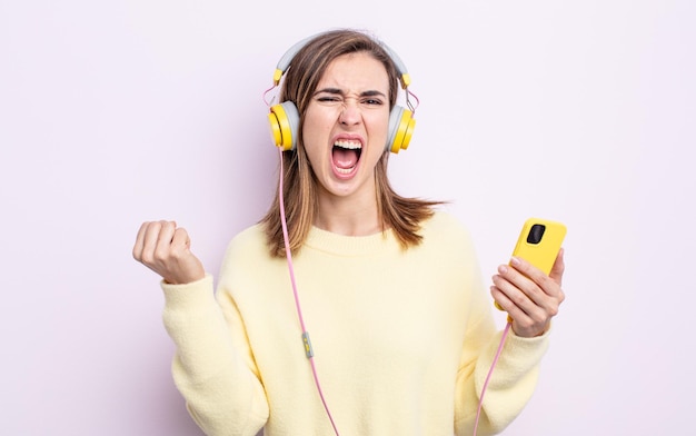 Jovem mulher bonita gritando agressivamente com uma expressão de raiva. fones de ouvido e conceito de telefone