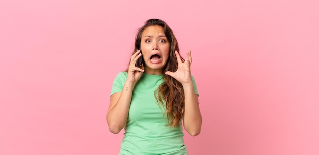 Jovem mulher bonita gritando com as mãos no ar e segurando um telefone inteligente