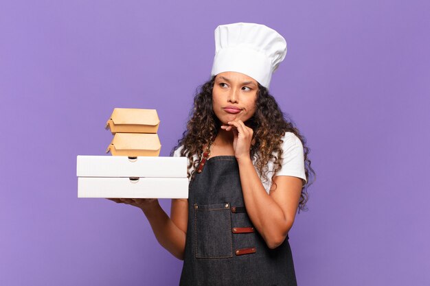 Jovem mulher bonita hispânica. pensando ou duvidando da expressão conceito do chef churrasco