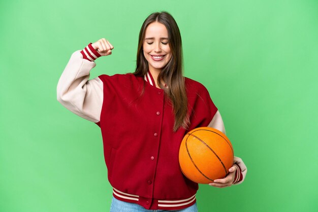 Jovem mulher bonita jogando basquete sobre fundo croma isolado fazendo gesto forte