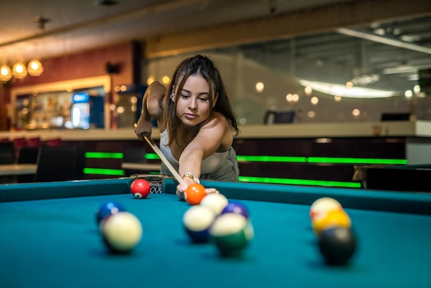 Jovem mulher bonita jogando sinuca sozinha segurando o taco na mesa de bilhar