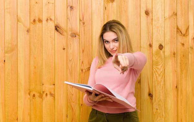 Jovem mulher bonita loira com livros contra a parede de madeira