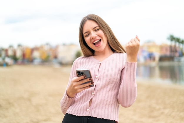 Jovem mulher bonita loira com telefone em posição de vitória