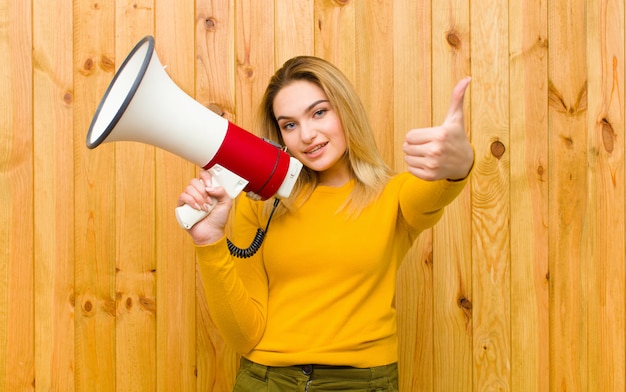 Jovem mulher bonita loira com um megafone na parede de madeira