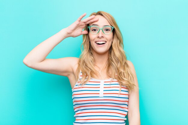 Jovem mulher bonita loira olhando feliz, surpreso e surpreso, sorrindo e percebendo boas notícias incríveis e incríveis contra a parede de cor lisa