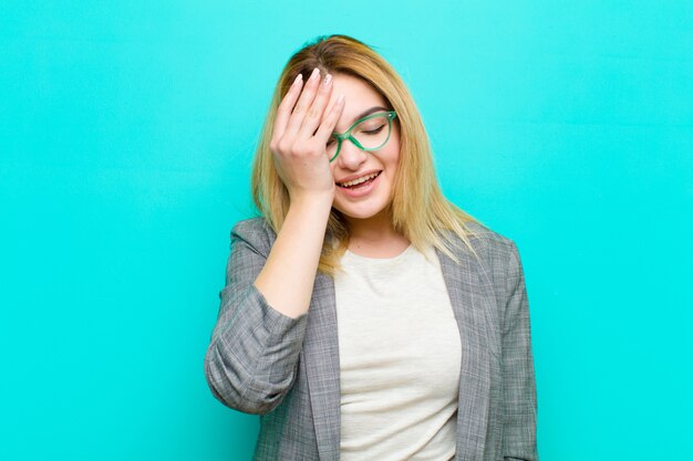 Jovem mulher bonita loira rindo e batendo na testa como dizer dãããããããão! Eu esqueci ou isso foi um erro estúpido contra parede plana