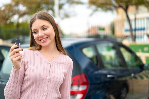 Jovem mulher bonita loira segurando as chaves do carro ao ar livre com expressão feliz