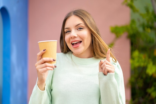 Jovem mulher bonita loira segurando um café para viagem ao ar livre apontando uma ótima ideia