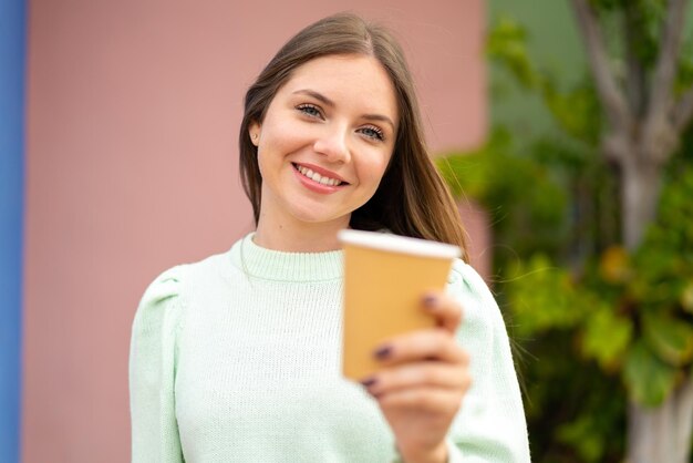 Jovem mulher bonita loira segurando um café para viagem com expressão feliz