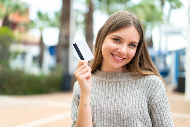 Jovem mulher bonita loira segurando um cartão de crédito com expressão feliz