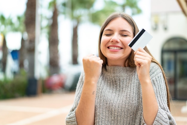 Foto jovem mulher bonita loira segurando um cartão de crédito e comemorando uma vitória