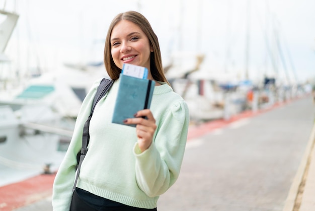 Jovem mulher bonita loira segurando um passaporte ao ar livre com expressão feliz