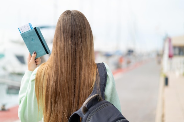 Jovem mulher bonita loira segurando um passaporte ao ar livre na posição traseira