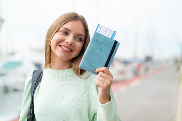 Jovem mulher bonita loira segurando um passaporte com expressão feliz