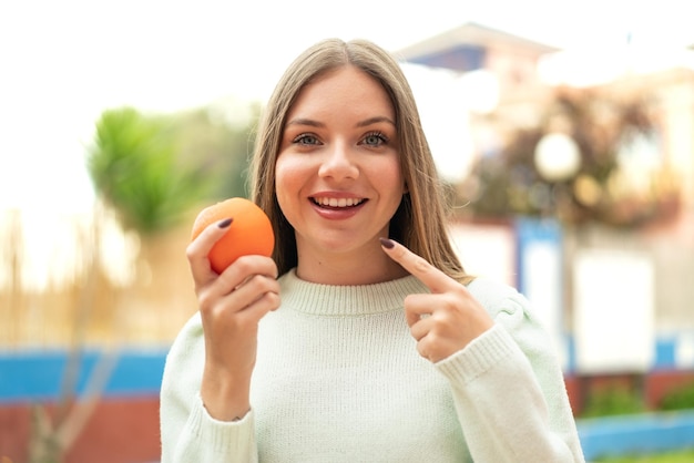 Jovem mulher bonita loira segurando uma laranja com expressão feliz