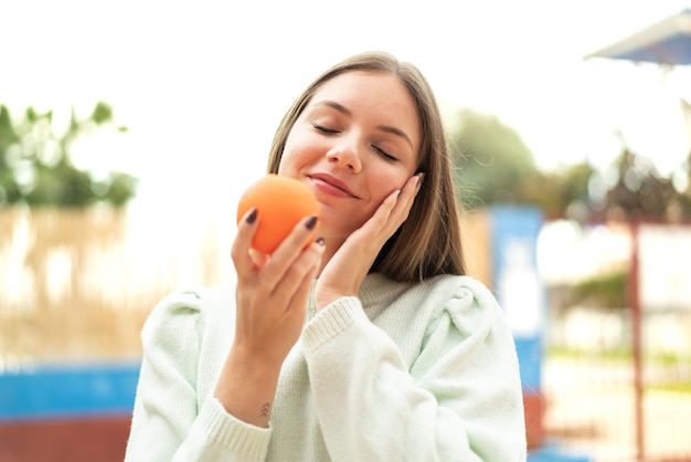 Jovem mulher bonita loira segurando uma laranja com expressão feliz