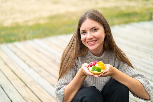 Jovem mulher bonita loira segurando uma tortinha com expressão feliz