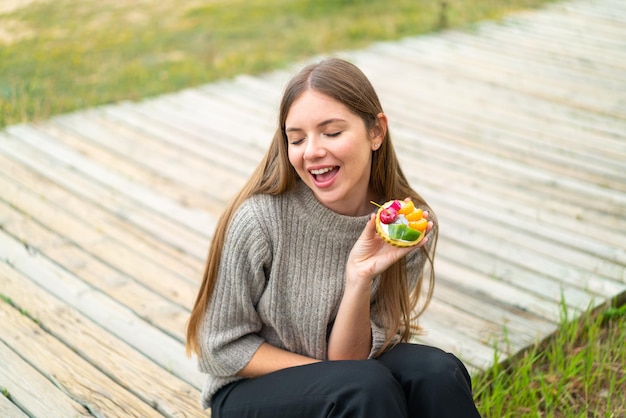 Jovem mulher bonita loira segurando uma tortinha com expressão feliz