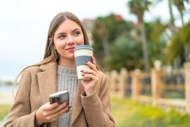 Jovem mulher bonita loira usando telefone celular e segurando um café