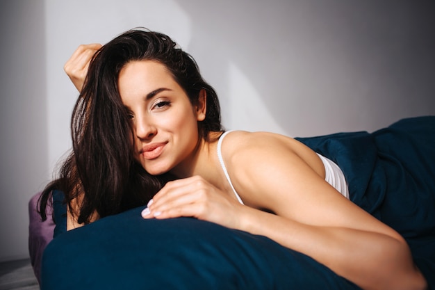 Jovem mulher bonita na cama de manhã em casa. Positivo modelo feminino sexy positivo alegre e sorriso. Morena gostosa na foto na sala ensolarada.