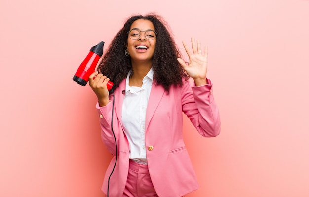 Jovem mulher bonita negra com um cabeleireiro contra parede rosa